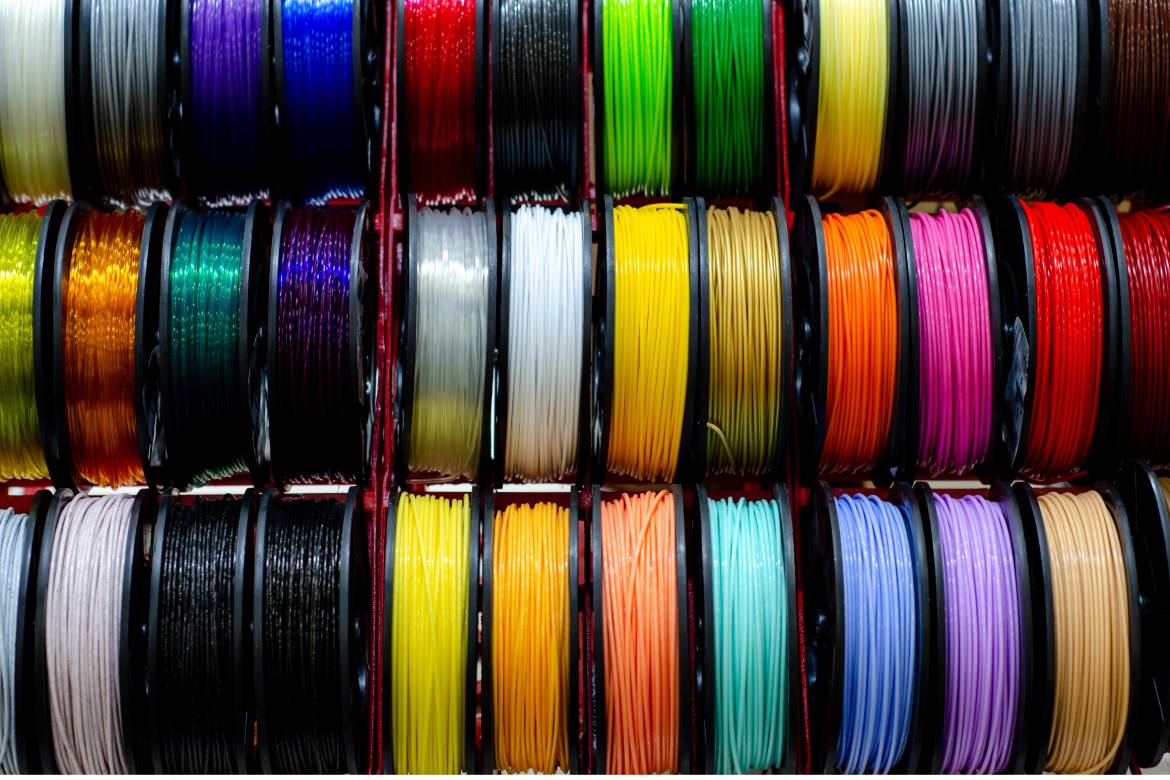 Three rows of thin pla filament spools for 3d printing in a wide assortment of colors, ranging from matte to shiny.