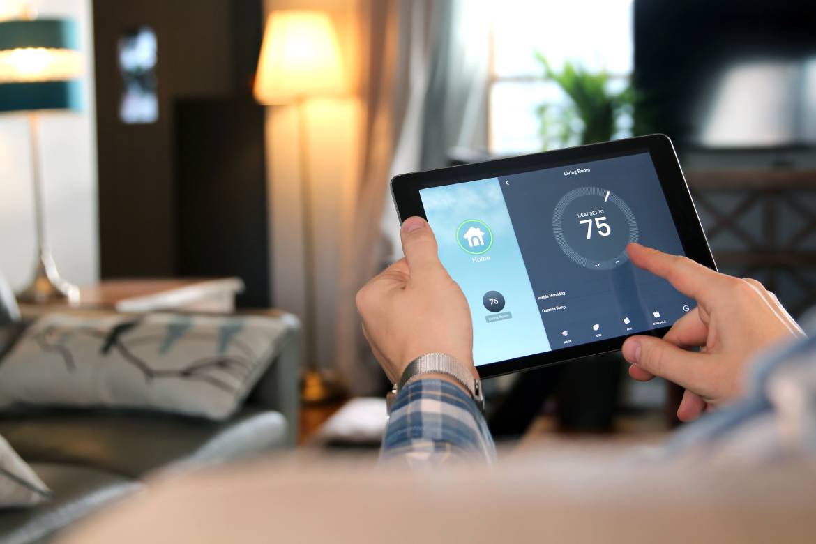 A man holding a touchscreen tablet that connects to his home thermostat. He adjusts the indoor temperature to 75 degrees.