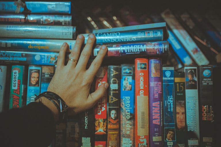 A hand reaching for a classic vhs tape from a colorful vintage collection indoors.