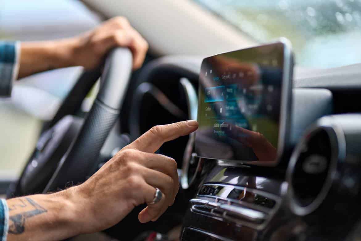 An older person sitting in a modern vehicle with a touchscreen navigation system. They're using the gps.