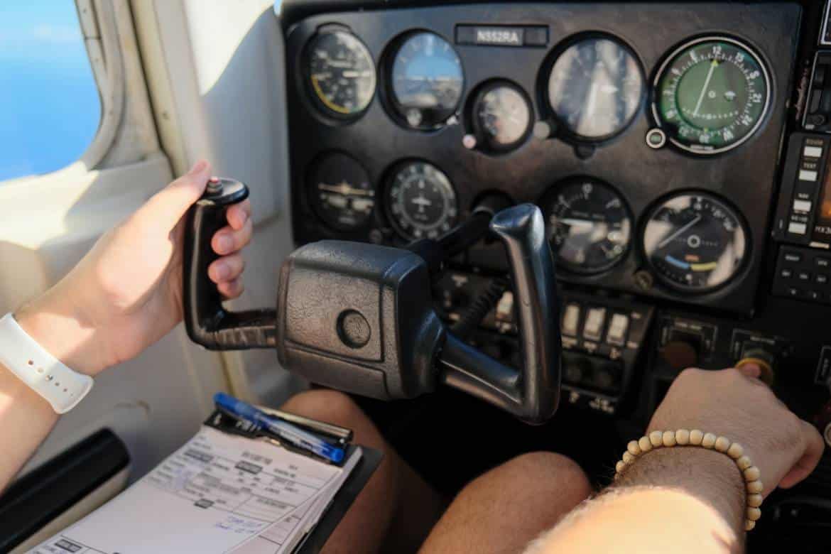 A pair of hands, up close, holding the yoke in a cessna's cockpit. Assorted gauges and switches are on full display.