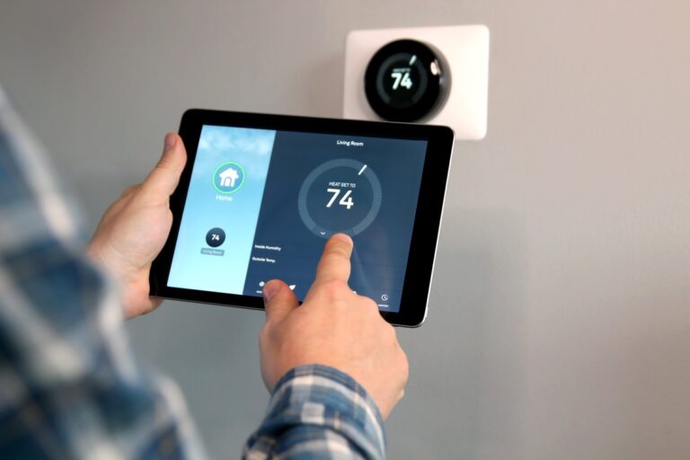 A homeowner using a tablet to control his smart home security settings. He's standing next to the smart thermostat.