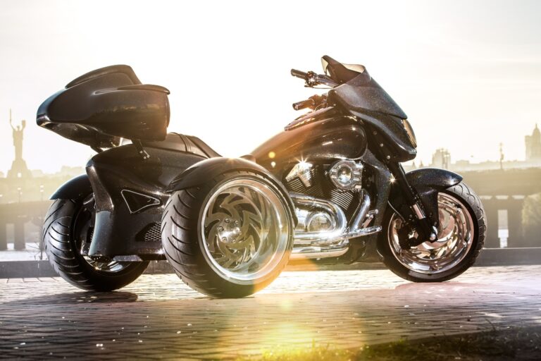 A black motor trike parked on the side of a road. There's a city skyline in the background and the sun is setting.