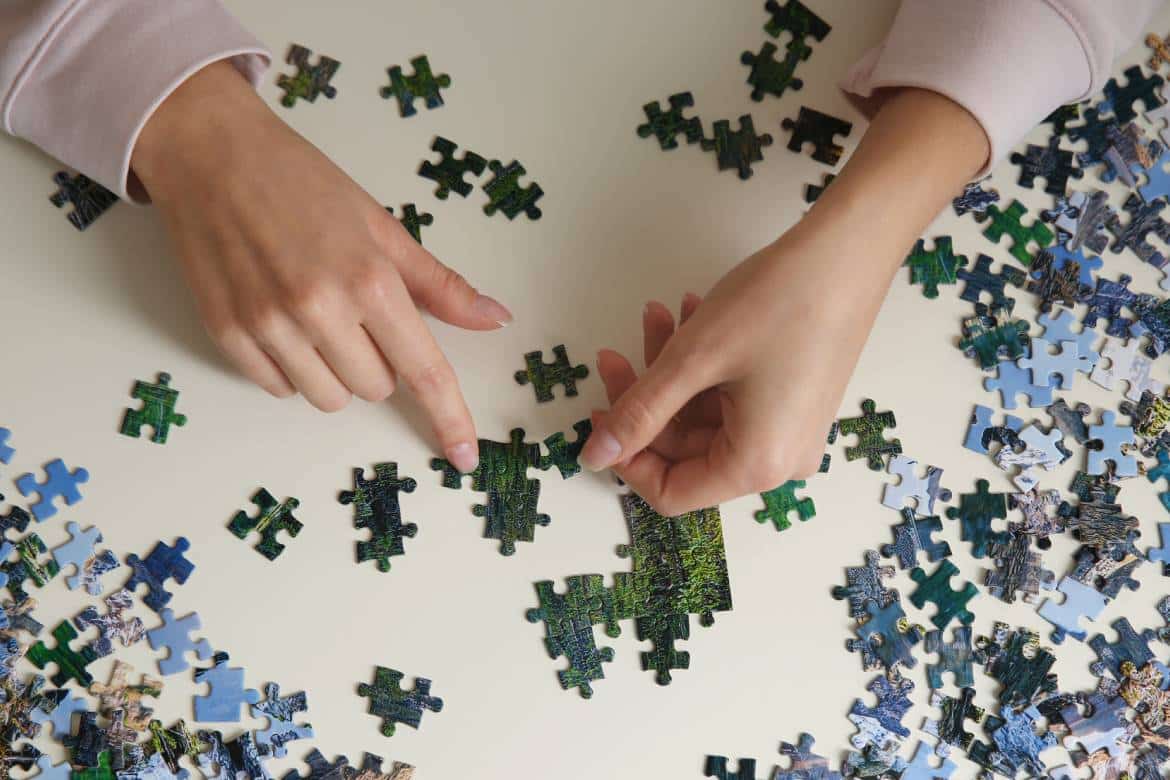A person using both hands to work on a large jigsaw puzzle. The puzzle pieces are small and only a handful are together.