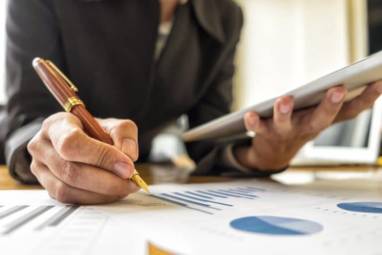 A professional investor sitting down at their desk with a tablet, a pen, and investment paperwork with a graph on it.