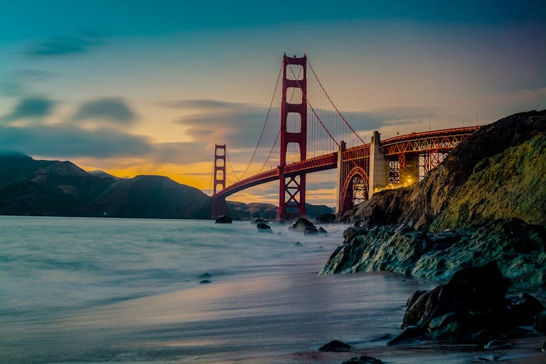 Stunning view of the golden gate bridge at dusk with ocean waves and dramatic sky.