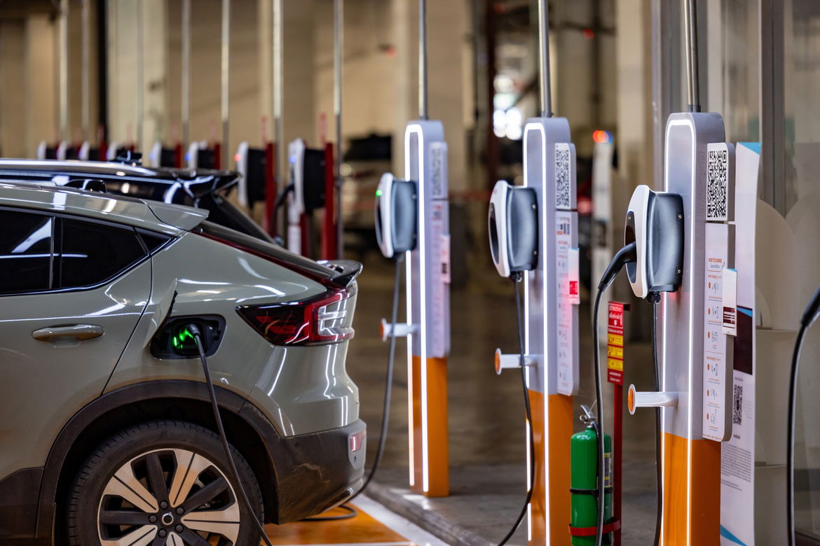 An electric vehicle parked beside a row of chargers with an adapter plugged into the lithium battery’s port.