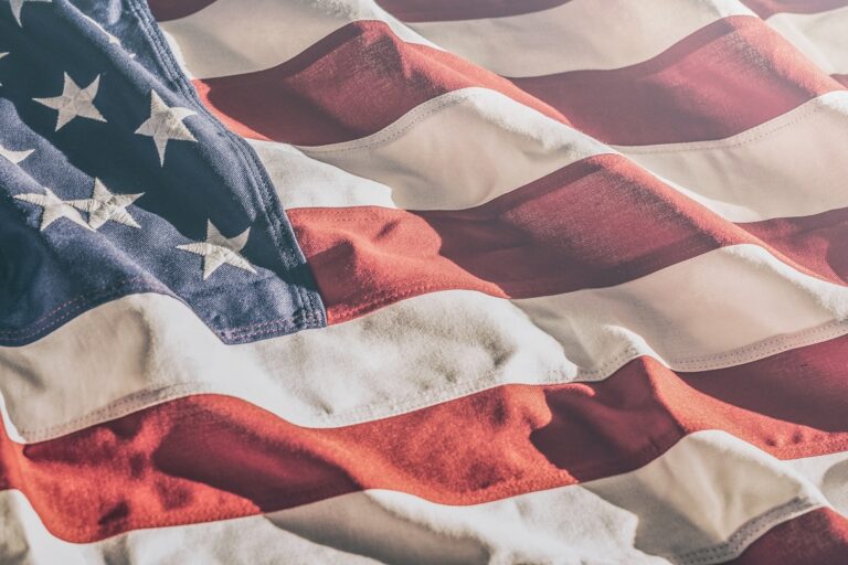 A close up of an american flag with wrinkles and folds as it waves in the sun. The coloring is slightly faded.