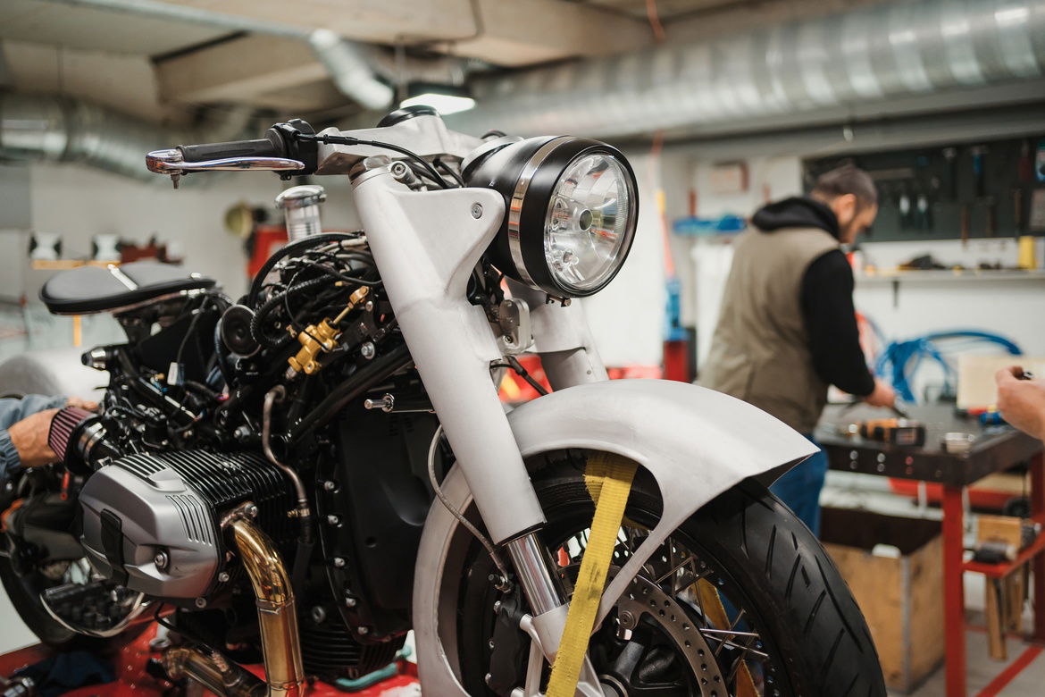 A motorcycle is secured with a yellow strap at a repair shop for tuning while the mechanic prepares tools.