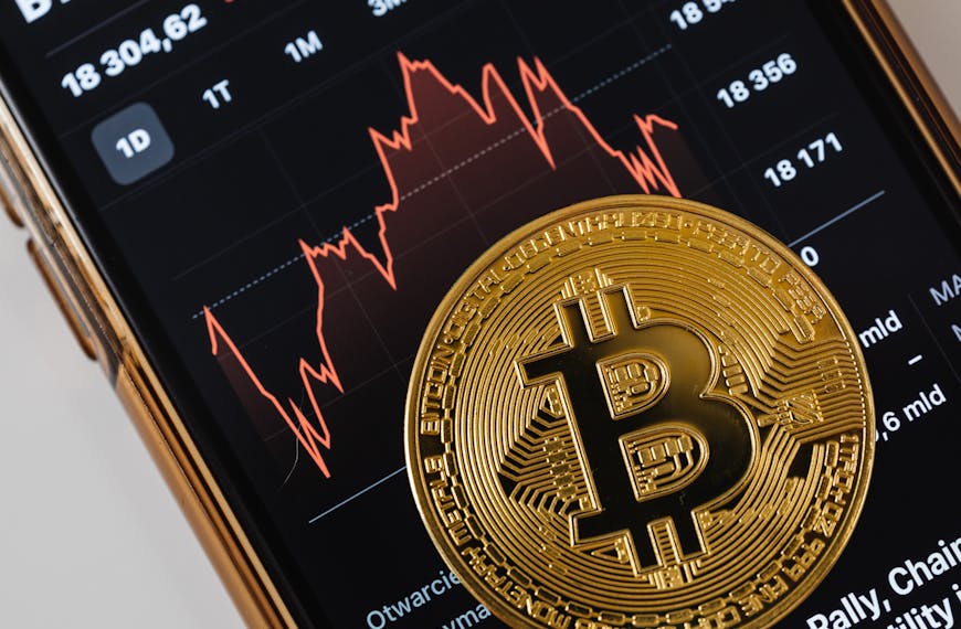 A close-up of a gold bitcoin coin placed on a smartphone displaying a stock market chart.