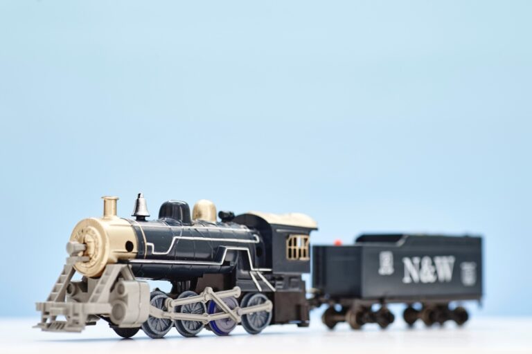 A navy toy train sits on a white surface against a baby blue background, with "n & w" printed on its wagon in white.
