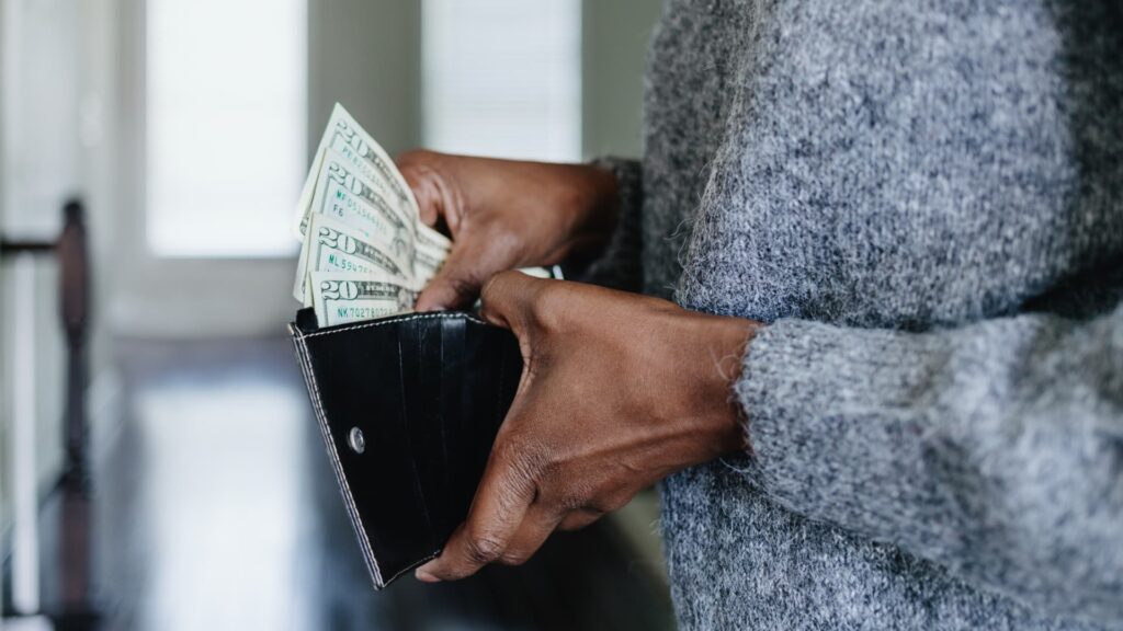 Geek insider how revenge saving is changing consumer habits forever 4 Close-up of hands adding money to a wallet as part of revenge saving goals.