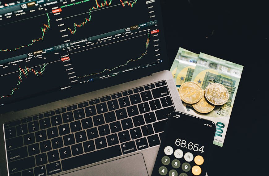 A laptop displaying stock charts with bitcoin, euros, and a cellphone calculator, showcasing financial analysis.