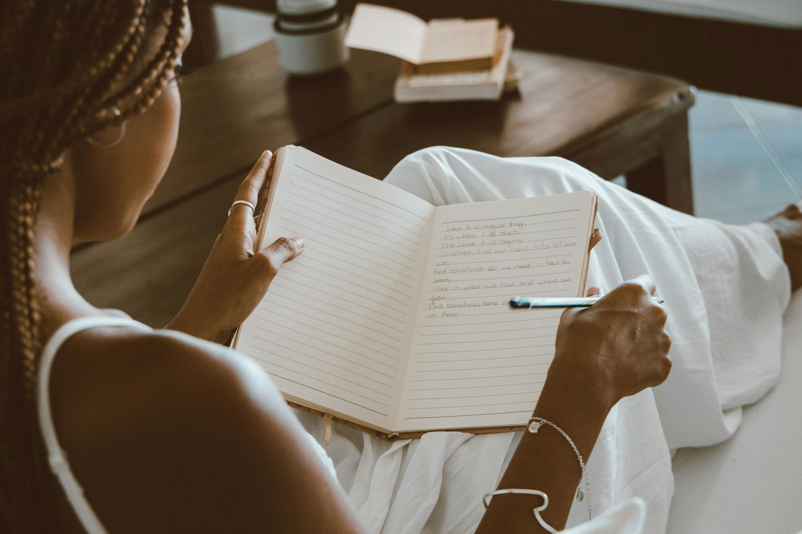 A black woman writes in a notebook, enjoying a calm indoor setting with natural light.