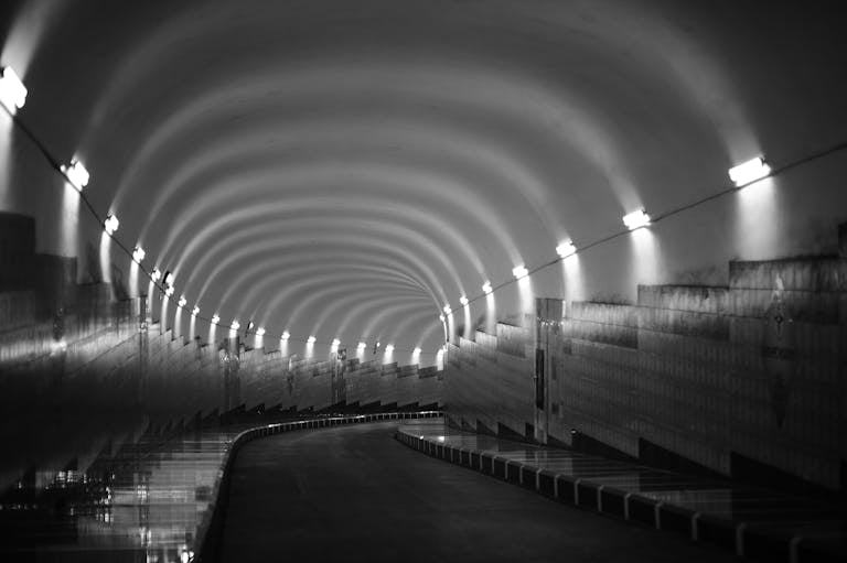 Moody black and white image of a tunnel with curved lighting and distinct shadows.