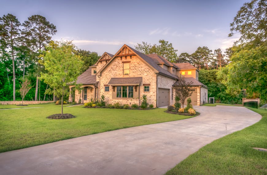 Elegant stone family home surrounded by trees, lush lawn, and vibrant garden.