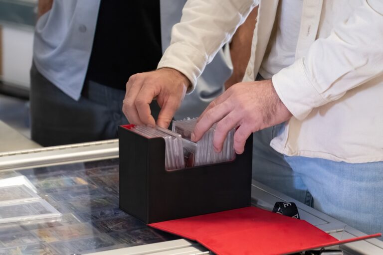 A close-up of a man wearing jeans and a white shirt, looking through a collection of cards next to someone else.