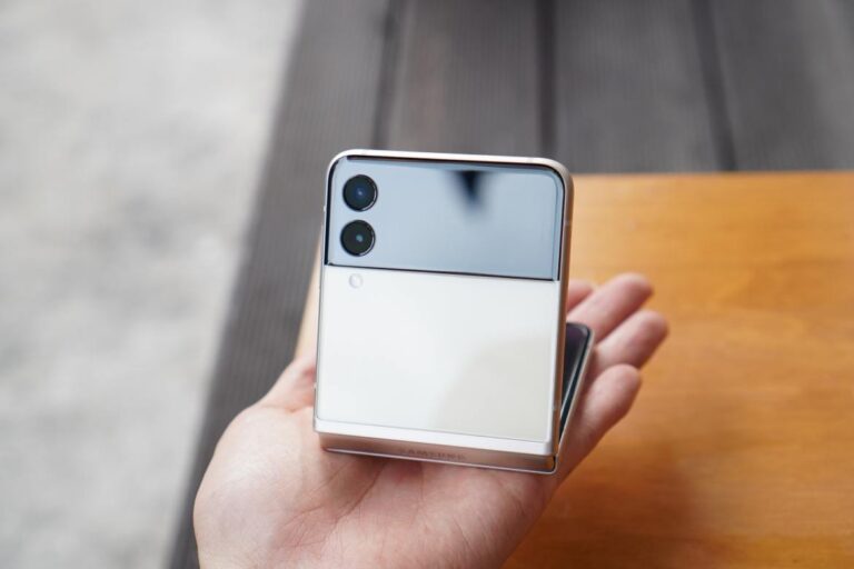 A person holding a half-folded smartphone with dual rear cameras and a reflective surface. The hinge is clearly visible.