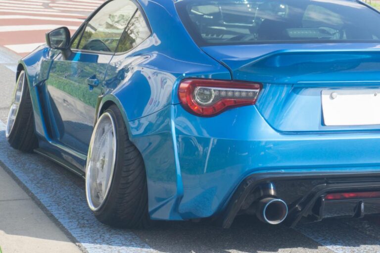 A rear view of a blue sports car featuring angled high-performance tires and an aggressive exhaust surround.