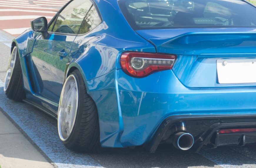 A rear view of a blue sports car featuring angled high-performance tires and an aggressive exhaust surround.