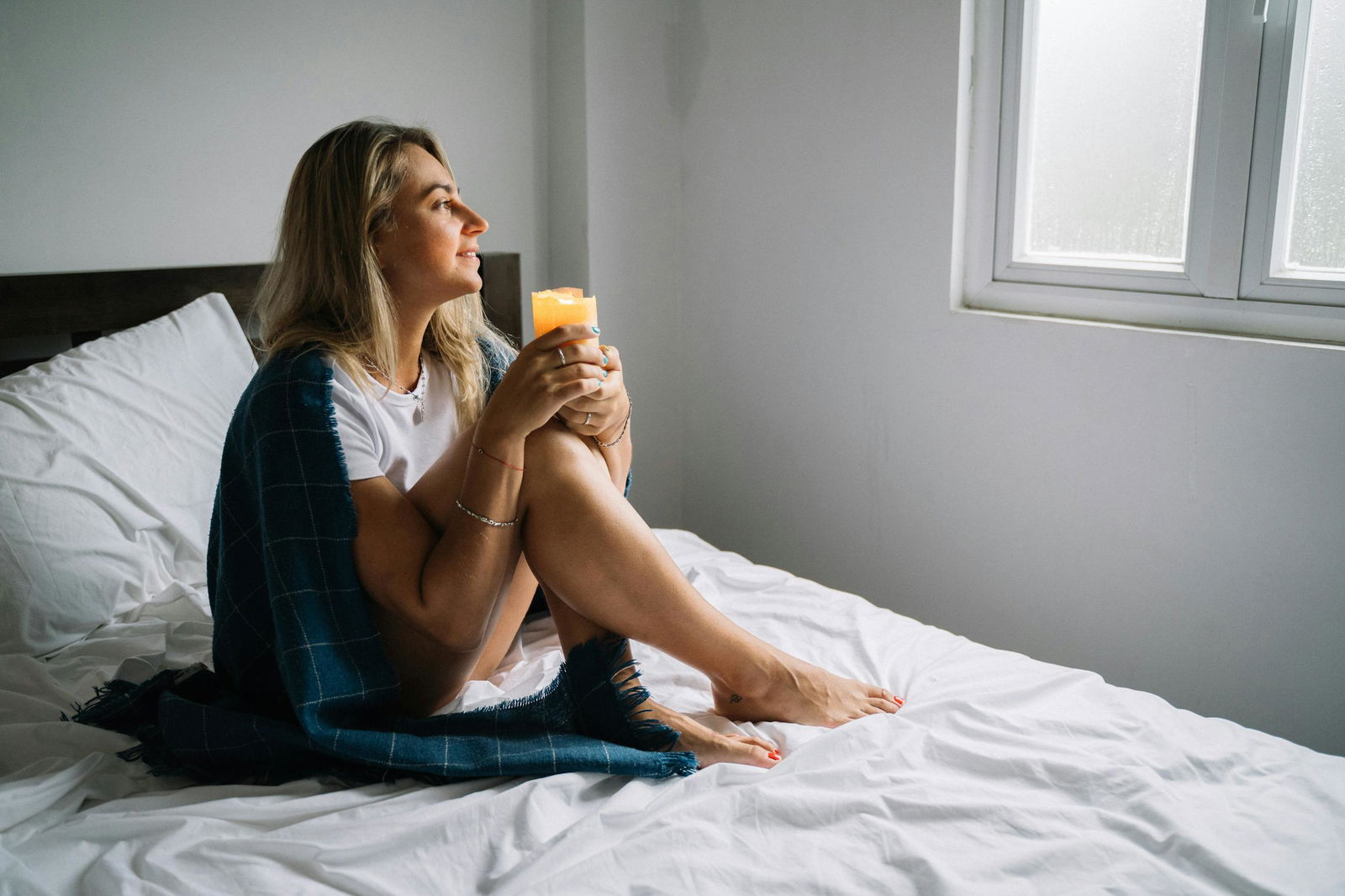 Woman sitting on bed with candle wrapped in a cozy blanket, enjoying morning tranquility.