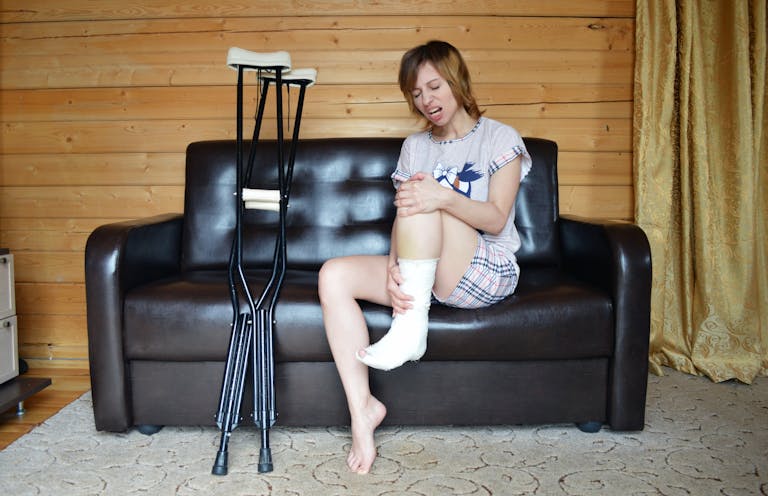 Young woman indoors with leg cast using crutches. Expressing discomfort and pain.