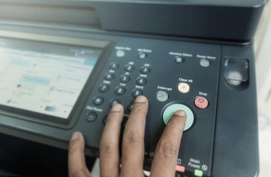 A close-up of a person pressing a green button on a printer’s control panel while a screen displays printer settings.