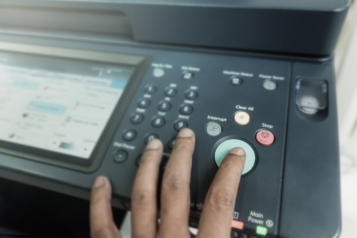 A close-up of a person pressing a green button on a printer’s control panel while a screen displays printer settings.