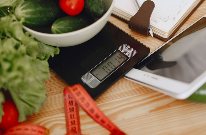 A bowl of fresh vegetables on a kitchen scale with measurement tools, depicting a healthy lifestyle.