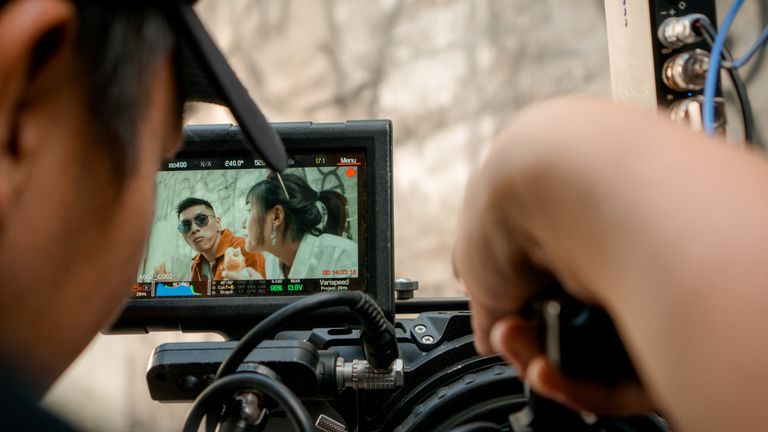Close-up of a video camera display filming an outdoor scene with a crew.